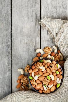 Wooden bowl with nuts on a wooden background, near a bag from burlap. Healthy food and snack, organic vegetarian food. Walnut, pistachios, almonds, hazelnuts and nuts of cashew, walnut. Top view.