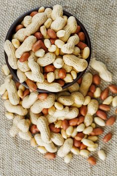 Peanuts in the shell and peeled close up in a cup. Background with peanuts. Roasted peanuts in the shell and peeled on a background of brown cloth in cups