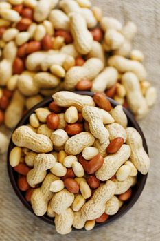 Peanuts in the shell and peeled close up in a cup. Background with peanuts. Roasted peanuts in the shell and peeled on a background of brown cloth in cups