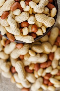 Peanuts in the shell and peeled close up in a cup. Background with peanuts. Roasted peanuts in the shell and peeled on a background of brown cloth in cups