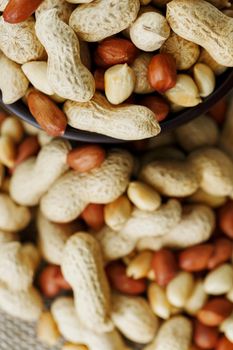 Peanuts in the shell and peeled close up in a cup. Background with peanuts. Roasted peanuts in the shell and peeled on a background of brown cloth in cups