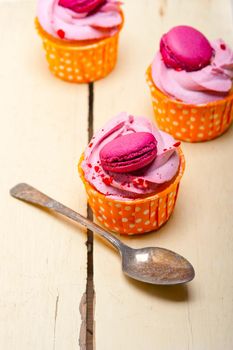 fresh pink berry cream cupcake with macaroon on top over rustic wood table