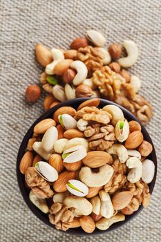 Mix of nuts of cashew, almonds, pistachios, hazelnuts and walnuts is against the background of brown fabric of burlap. Nuts as structure and background, macro