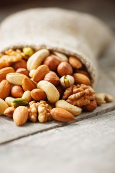 Mix of nuts of cashew, almonds, pistachios, hazelnuts and walnuts is against the background of brown fabric of burlap. Nuts as structure and background, macro