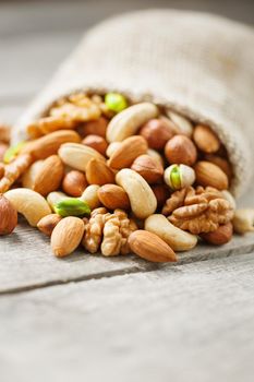 Mix of nuts of cashew, almonds, pistachios, hazelnuts and walnuts is against the background of brown fabric of burlap. Nuts as structure and background, macro