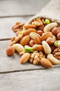 Mix of nuts of cashew, almonds, pistachios, hazelnuts and walnuts is against the background of brown fabric of burlap. Nuts as structure and background, macro