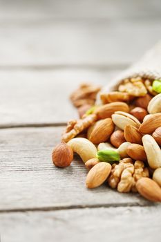 Mix of nuts of cashew, almonds, pistachios, hazelnuts and walnuts is against the background of brown fabric of burlap. Nuts as structure and background, macro