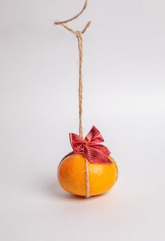 Festive tangerine with a red bow hanging from a rope. Holiday concept New Year.