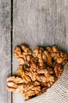 Walnuts in a burlap bag on a wooden background. Walnut macro - edible kernels of seeds. Healthy and healthy food for vegetarians