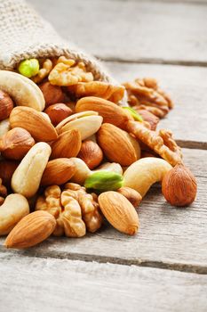 Mix of nuts of cashew, almonds, pistachios, hazelnuts and walnuts is against the background of brown fabric of burlap. Nuts as structure and background, macro