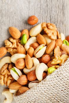 Mix of nuts of cashew, almonds, pistachios, hazelnuts and walnuts is against the background of brown fabric of burlap. Nuts as structure and background, macro