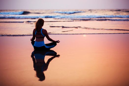 Young healthy woman practicing yoga on the beach at sunset