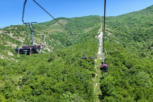 Chairlift going up the mountain. Beautiful sunset on the mountains full of trees, orange, green and blue behind the chairlift.