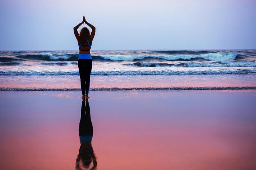 Young healthy woman practicing yoga on the beach at sunset