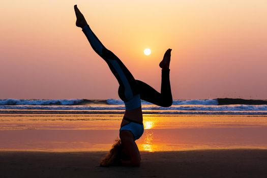 Young healthy woman practicing yoga on the beach at sunset