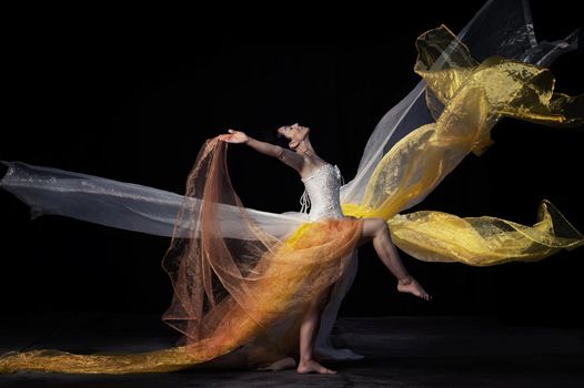 beautiful woman of Caucasian appearance with black hair dances on a black background. Woman wearing white corset and skirt, passion pose