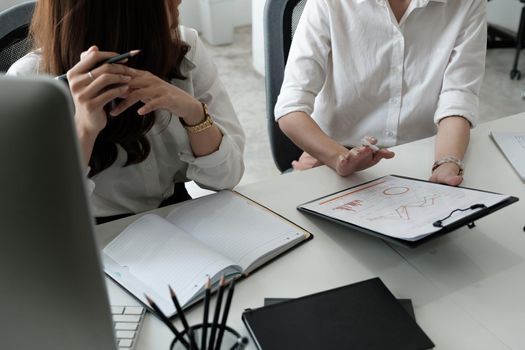 Close up two young woman working together on paperwork chart graph report. Creative female executives meeting in a office using pc