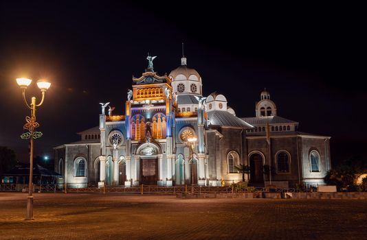 Nigh photo of illuminated Basilica de Nuestra Senora de los Angeles (Our Lady of the Angels Basilica). Roman Catholic basilica in Costa Rica, located in Cartago and dedicated to Lady of the Angels