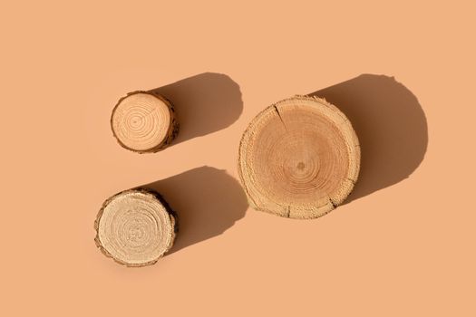 Three wooden disks lying on a trendy beige background. A platform made of trees for luxury and natural cosmetics or products presentation. Wood tray mockup in the sunlight. Top view