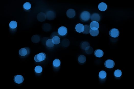 Defocused bokeh lights on black background, an abstract naturally blurred backdrop for Christmas eve or birthday party. Festive light texture. Blue garland in blur. Overlay effect for design