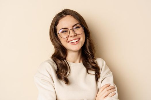 Close up portrait of young caucasian woman with dark hair, smiling white teeth, laughing, posing carefree against beige background.