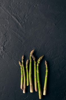 Green raw asparagus spears on black slate background. Concept of healthy food and crop of spring vegetables. Close up, copy space. Flat lay, top view