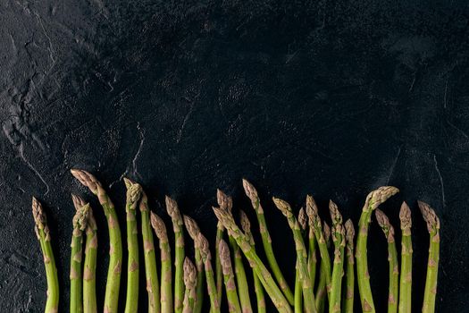 Raw uncooked green asparagus spears on black slate background. Concept of healthy nutrition, food and seasonal vegetables harvest. Close up, copy space. Flat lay, top view