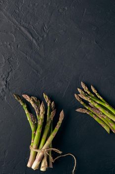 Fresh green asparagus spears in bunch are tied with jute thread on black slate background. Concept of healthy nutrition, food and seasonal vegetables harvest. Close up, copy space. Flat lay, top view