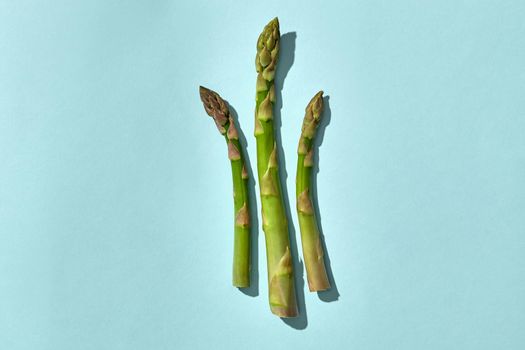 Three green asparagus spears on blue background. Concept of healthy food and seasonal vegetables harvest. Close up, copy space. Flat lay, top view