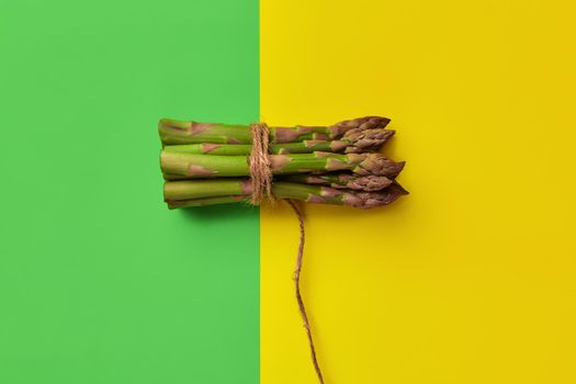 Fresh asparagus spears in bunch are tied with jute thread over yellow and green background. Healthy nutrition, food and seasonal vegetables harvest. Close up, copy space. Flat lay, top view