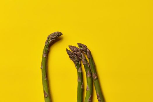 Four raw green asparagus stems over yellow background. Concept of healthy nutrition, food and seasonal vegetables harvest. Close up, copy space. Flat lay, top view