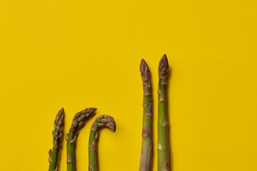 Raw uncooked green asparagus spears on yellow background. Concept of healthy nutrition, food and seasonal vegetables harvest. Close up, copy space. Flat lay, top view