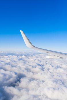 View of airplane white wing flying in blue sky over clouds. Travel concept