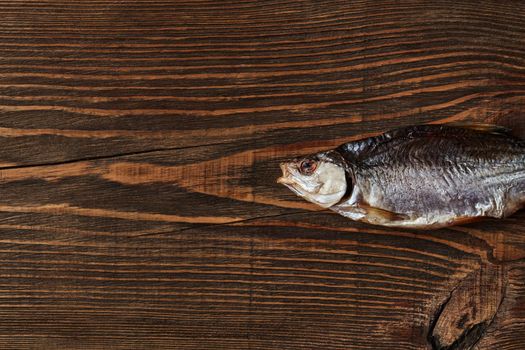 One dried or jerky salted roach, tasty clipfish on wooden background. Salty beer appetizer. Traditional way of preserving fish. Close up, top view