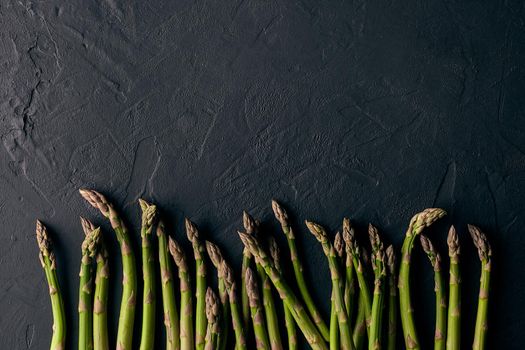 Raw fresh green asparagus stalks over black slate background. Concept of food and seasonal vegetables harvest. Close up, copy space. Flat lay, top view