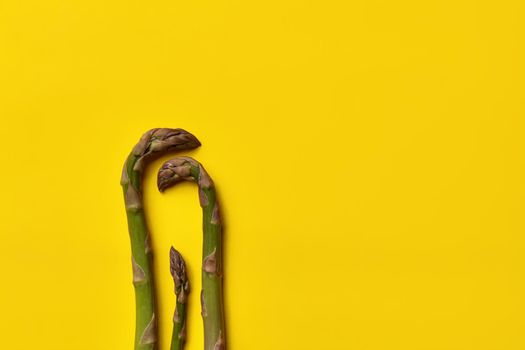 Three uncooked green asparagus spears over yellow background. Concept of healthy nutrition, food and seasonal vegetables harvest. Close up, copy space. Flat lay, top view