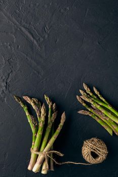 Ripe raw asparagus stalks in bunch are tied with jute thread on black slate background. Healthy nutrition, food and seasonal vegetables harvest. Close up, copy space. Flat lay, top view