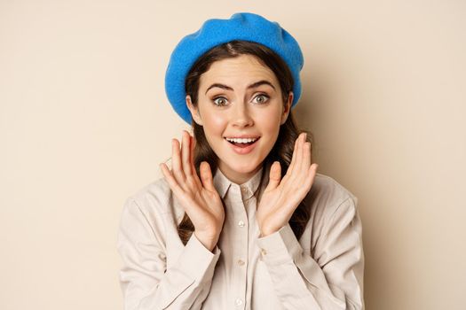 Close up portrait of woman looking surprised, amazed reaction at big news, special deal, standing over beige background.