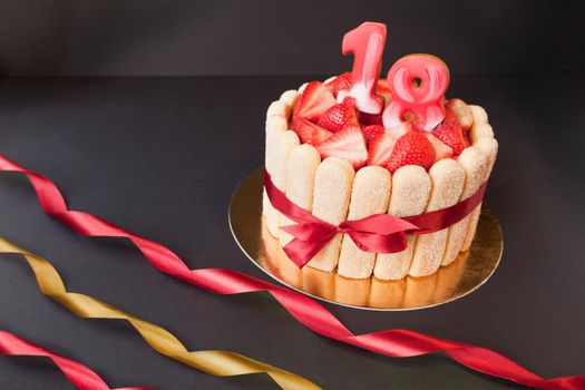 18 birthday party tart. strawberry tiramisu cake on black background with golden and red ribbon. Focus on strawberries.