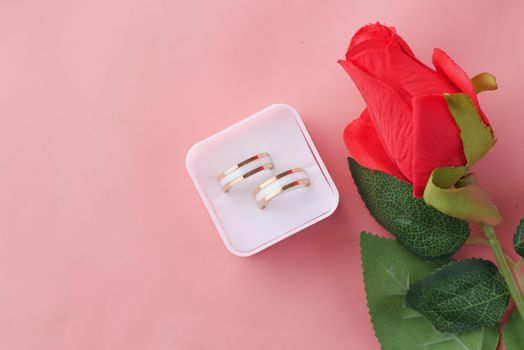 wedding ring and gift box and rose flower on red .