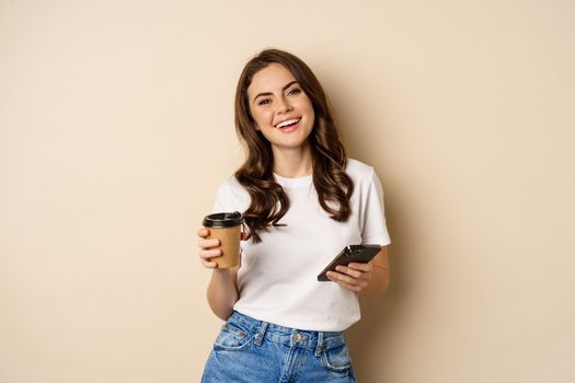 Smiling woman using mobile phone app and credit card, concept of online shopping, contactless payment and delivery, standing over beige background.