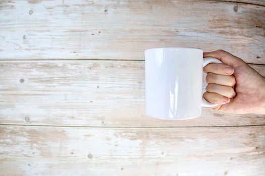 Hand holding a ceramic mug blank on wooden background with copy space, space for text