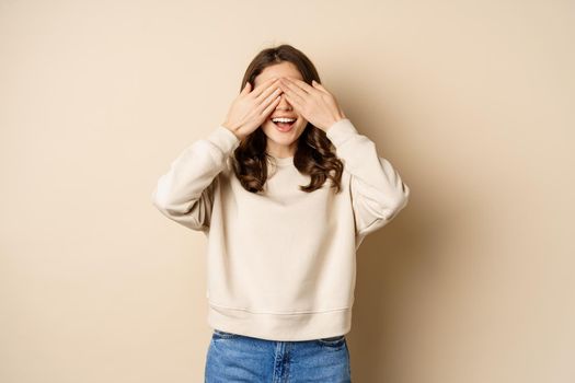 Excited happy girl smiling, close eyse and wait for surprise gift, standing blinsided over beige background.