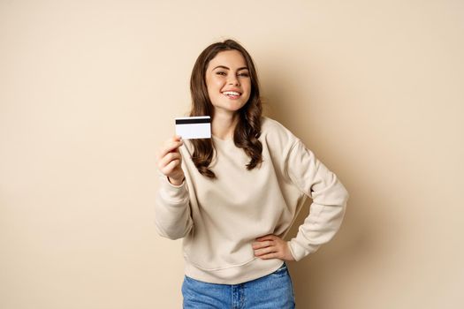 Happy woman customer showing credit card, smiling satisfied, standing over beige background.