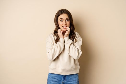 Portrait of woman looking with interest and yearning, biting finger, wants to try taste smth, standing over white background.