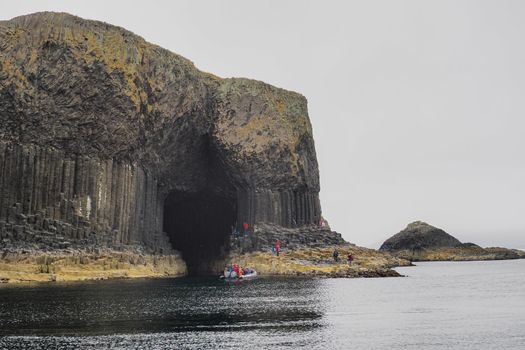 Tourists with boat visit Fingals Cave and hexagonal volcanic basalt rock columns, Isle of Staffa, Hebrides, Scotland, UK