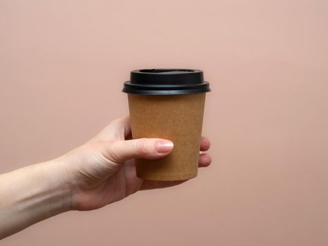 Woman hands hold paper cup on pink background. Copy space.