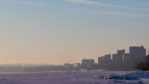 Coast of the winter river in Siberia. Skyline with outlines of houses and steam above the water