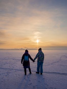 Two girls go into the sunset along the frozen river