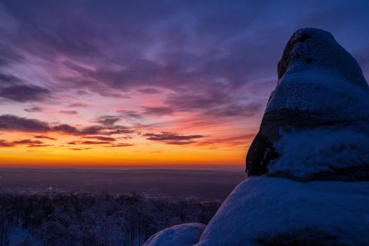 Epic red sunset over the rocks and stones of Ural mountains covered with snowy pines